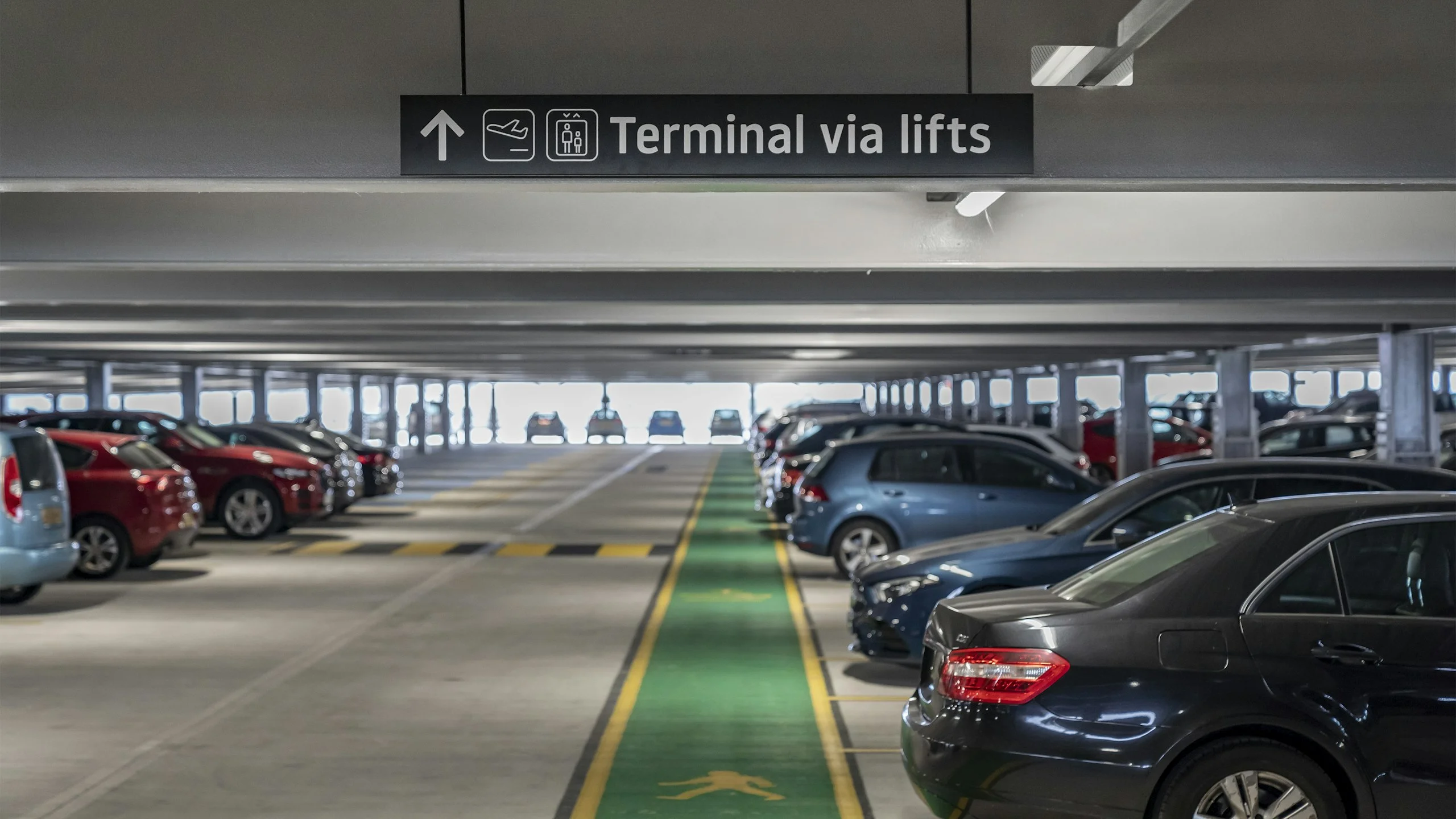 Multi-storey car park with columns, parked cars and a marked walkway